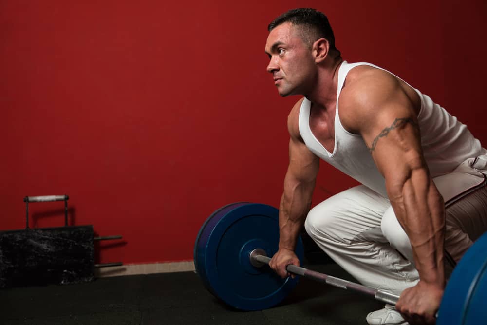 A man in white gym attire prepares to perform a deadlift with proper form to avoid suffering a back injury.