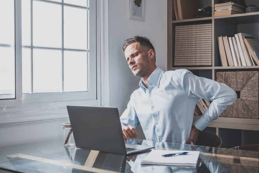 A man sits at his computer researching how to sit with sciatica while experiencing intense sciatica pain.