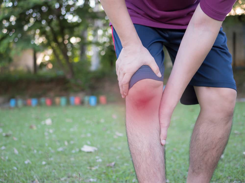 A man with arthritis in his knee reaches down and reels from the pain visualized by a red aura over his kneecap.